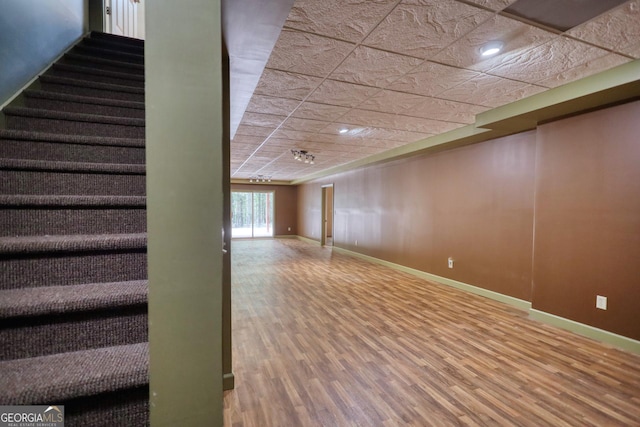 below grade area with stairs, baseboards, a drop ceiling, and wood finished floors