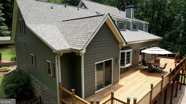 rear view of house with roof with shingles, a chimney, a wooden deck, and outdoor dining space