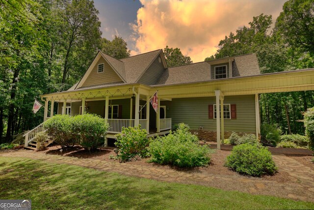 back house at dusk featuring a yard and covered porch