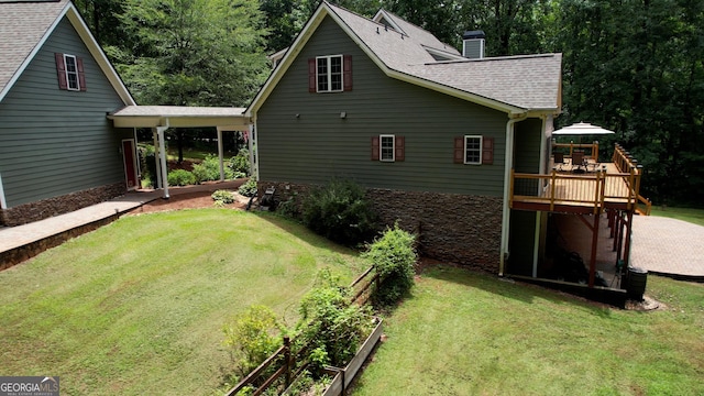 back of house with a deck, roof with shingles, a yard, and a chimney