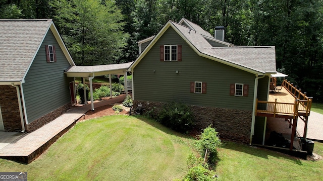 rear view of property with a shingled roof, a chimney, a deck, and a yard