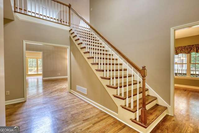 stairway featuring baseboards, visible vents, a high ceiling, and wood finished floors