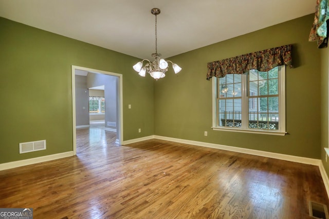 unfurnished dining area with a healthy amount of sunlight, visible vents, a notable chandelier, and wood finished floors