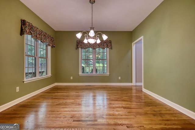 unfurnished dining area featuring baseboards, wood finished floors, and a notable chandelier