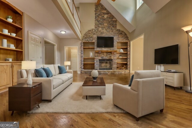 living room featuring built in features, a fireplace, light hardwood / wood-style flooring, and a high ceiling