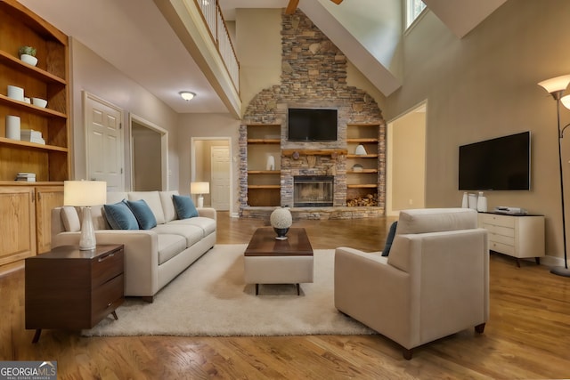 living room with light wood finished floors, baseboards, built in features, and a stone fireplace