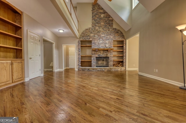 unfurnished living room with built in features, a stone fireplace, hardwood / wood-style floors, and a towering ceiling