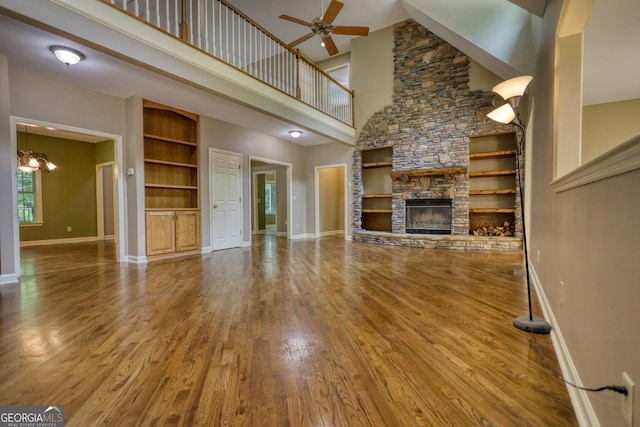 unfurnished living room with baseboards, ceiling fan with notable chandelier, wood finished floors, and built in features