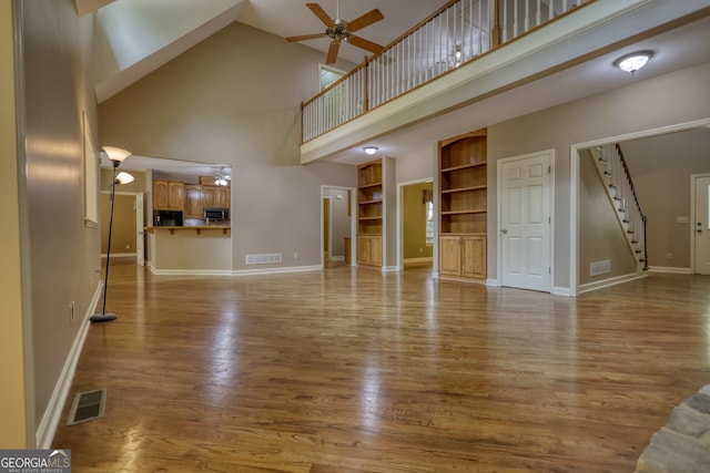 unfurnished living room featuring ceiling fan, built in shelves, light hardwood / wood-style flooring, and high vaulted ceiling