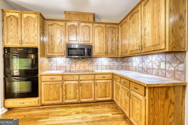 kitchen featuring black appliances, tasteful backsplash, light wood-type flooring, and tile counters