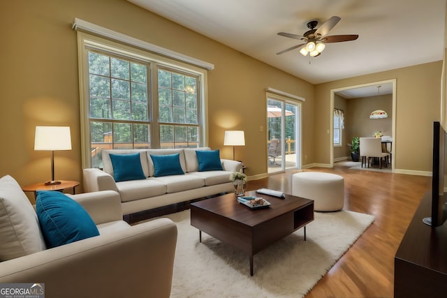 living area featuring ceiling fan, light wood-style flooring, and baseboards