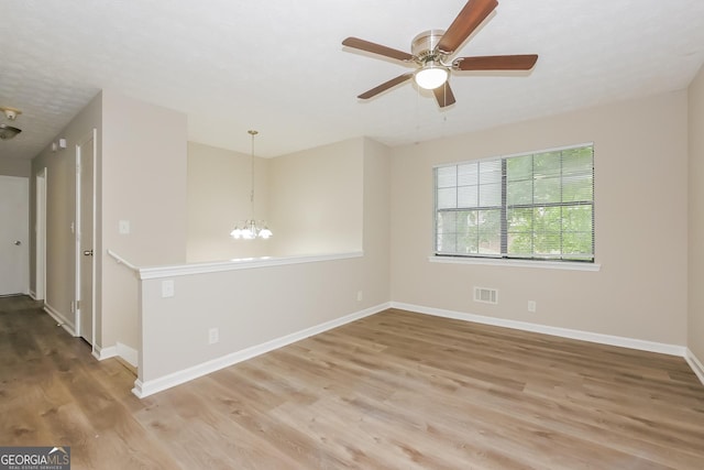 unfurnished room with ceiling fan with notable chandelier and light hardwood / wood-style floors