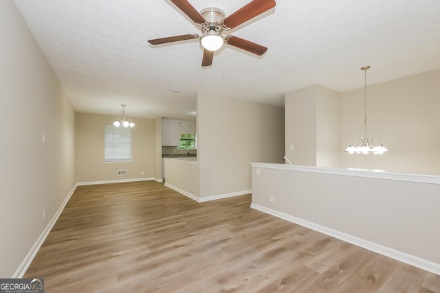 unfurnished room featuring ceiling fan with notable chandelier, a textured ceiling, and light wood-type flooring