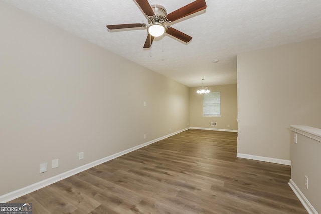 empty room with ceiling fan with notable chandelier, dark hardwood / wood-style floors, and a textured ceiling