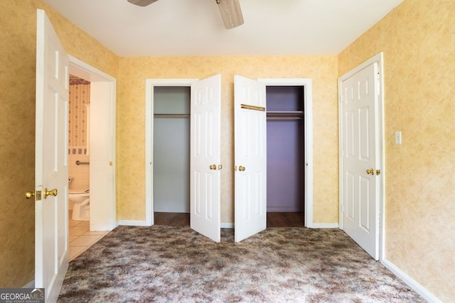 unfurnished bedroom with two closets, ensuite bath, ceiling fan, and tile patterned floors