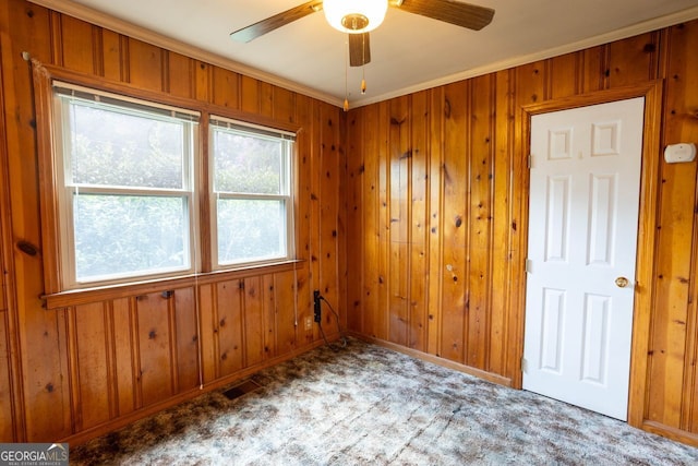 spare room with ornamental molding, carpet flooring, ceiling fan, and wooden walls