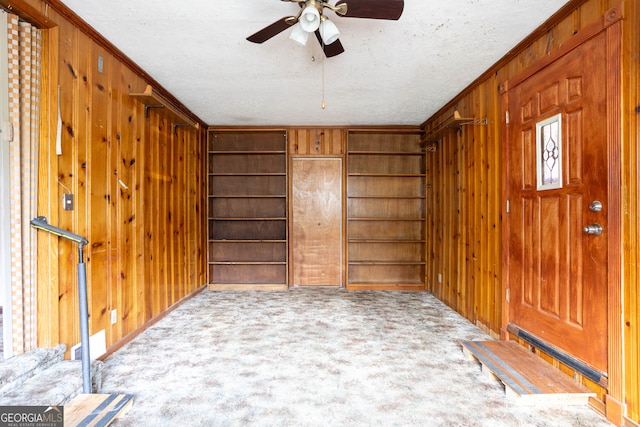 foyer entrance featuring wooden walls, crown molding, carpet, and ceiling fan