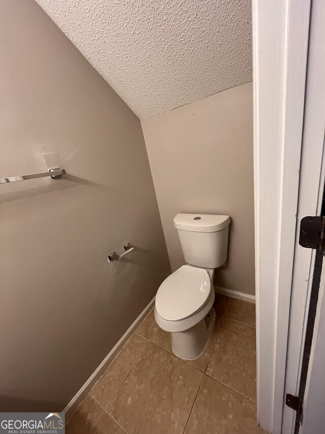 bathroom with toilet, tile patterned floors, a textured ceiling, and lofted ceiling