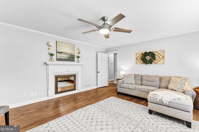 living room featuring ornamental molding, wood-type flooring, ceiling fan, and a fireplace