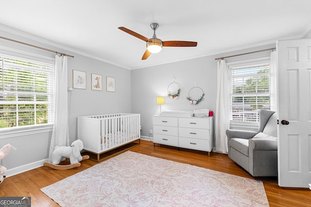 bedroom with ceiling fan, ornamental molding, hardwood / wood-style floors, and a crib