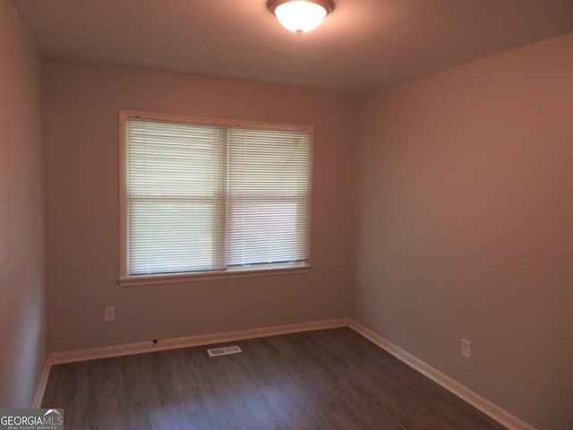 empty room featuring dark wood-type flooring and a healthy amount of sunlight