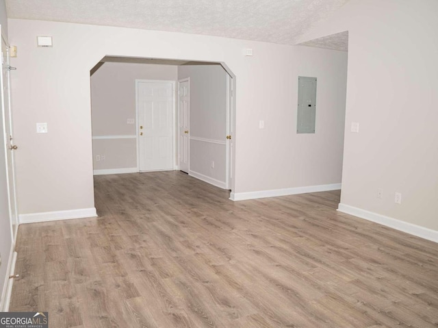 empty room with a textured ceiling, electric panel, and hardwood / wood-style flooring