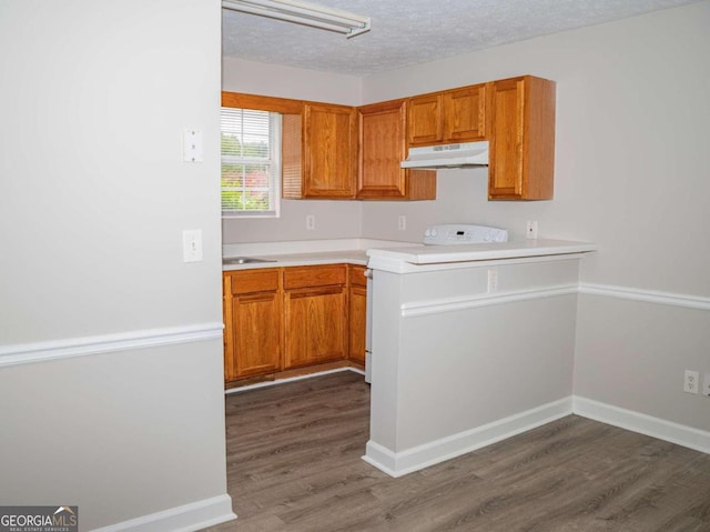 kitchen with white electric range oven, kitchen peninsula, a textured ceiling, dark hardwood / wood-style floors, and sink