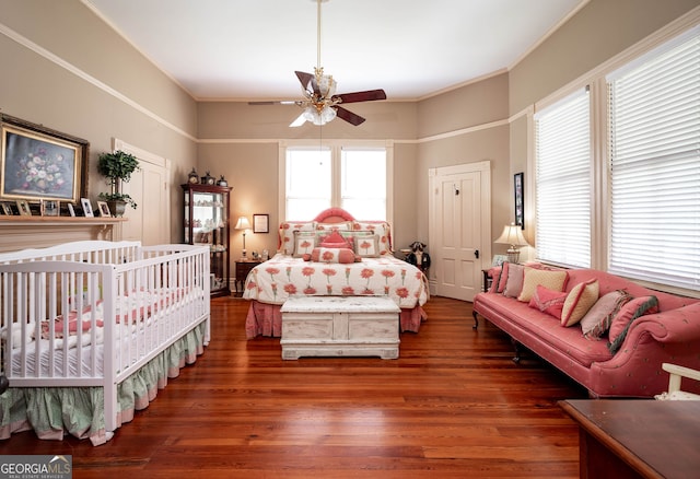 bedroom with multiple windows, a nursery area, ceiling fan, and hardwood / wood-style floors