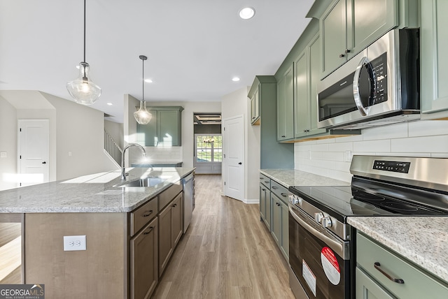 kitchen featuring pendant lighting, a kitchen island with sink, green cabinets, light stone countertops, and stainless steel appliances