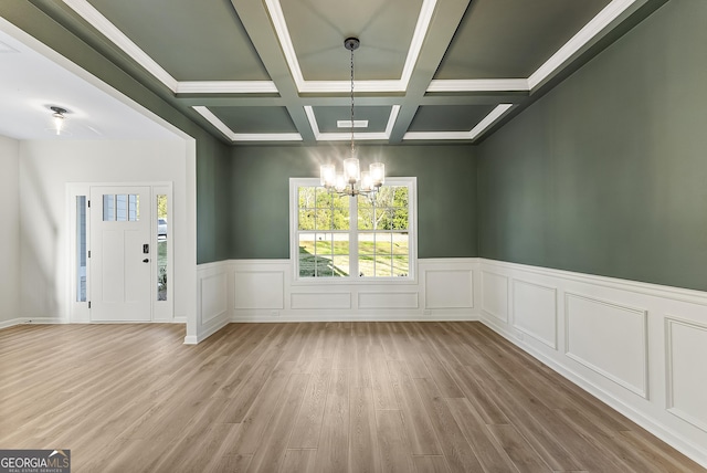 empty room with beam ceiling, coffered ceiling, an inviting chandelier, crown molding, and light wood-type flooring