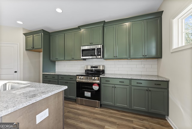 kitchen featuring light stone countertops, backsplash, stainless steel appliances, and green cabinetry