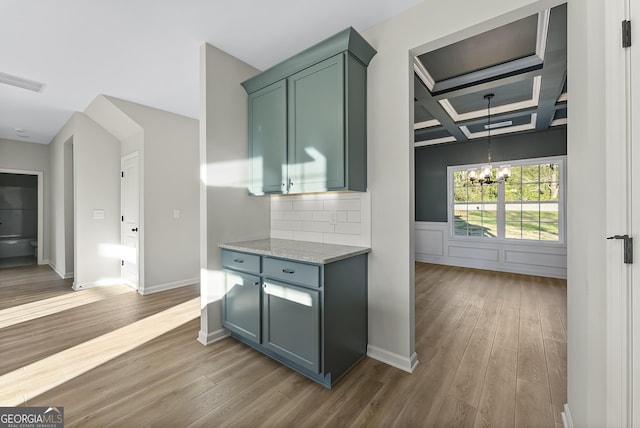 kitchen featuring light stone countertops, light wood-type flooring, tasteful backsplash, coffered ceiling, and an inviting chandelier