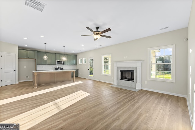 unfurnished living room featuring ceiling fan, a healthy amount of sunlight, light wood-type flooring, and a fireplace