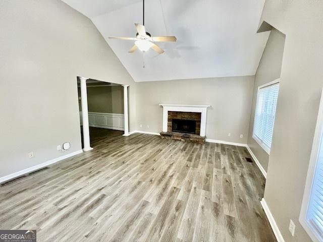 unfurnished living room featuring ceiling fan, high vaulted ceiling, a stone fireplace, and light hardwood / wood-style floors