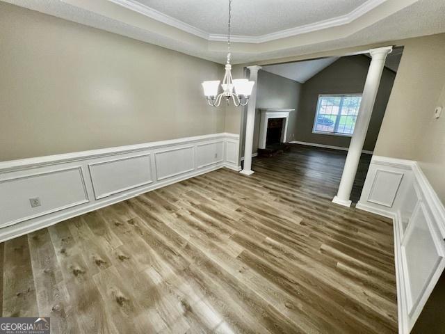 unfurnished dining area with lofted ceiling, crown molding, wood-type flooring, and decorative columns