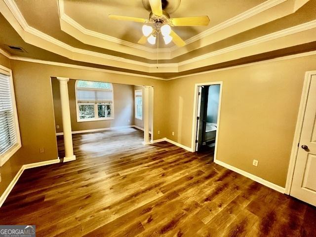 spare room with a raised ceiling, crown molding, dark wood-type flooring, and decorative columns