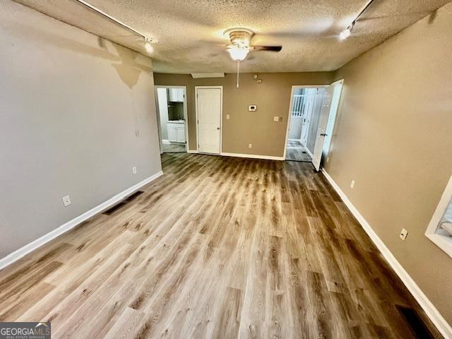 spare room with wood-type flooring, rail lighting, ceiling fan, and a textured ceiling