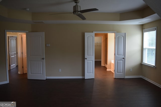 unfurnished bedroom with ceiling fan, a walk in closet, and dark hardwood / wood-style flooring