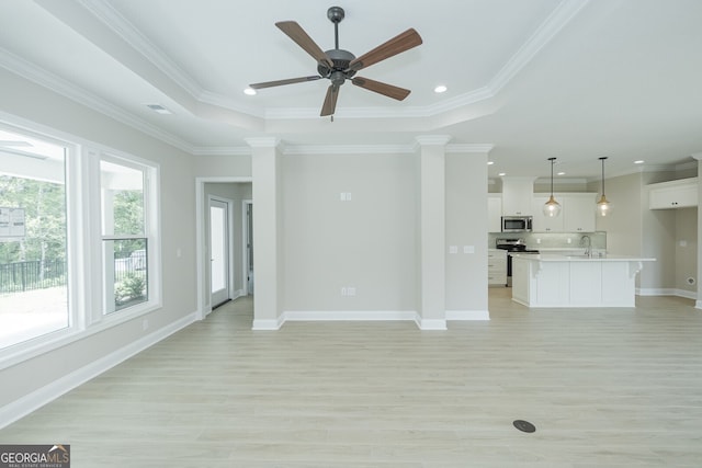 unfurnished living room with a tray ceiling, decorative columns, light hardwood / wood-style floors, crown molding, and ceiling fan