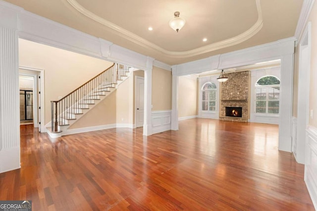 unfurnished living room featuring crown molding, a stone fireplace, a raised ceiling, and hardwood / wood-style flooring