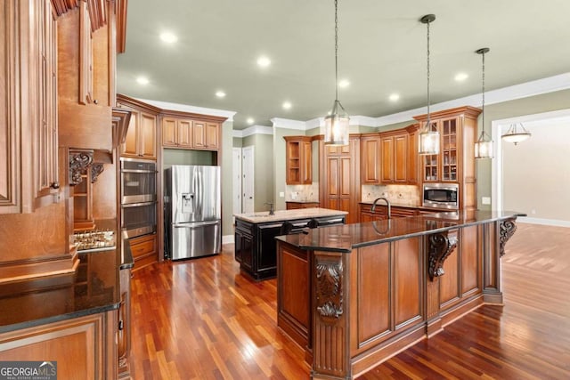 kitchen with hanging light fixtures, a center island with sink, appliances with stainless steel finishes, ornamental molding, and decorative backsplash