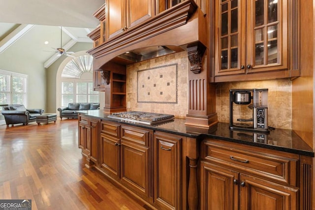 kitchen with ceiling fan, dark stone countertops, wood-type flooring, stainless steel gas cooktop, and custom exhaust hood