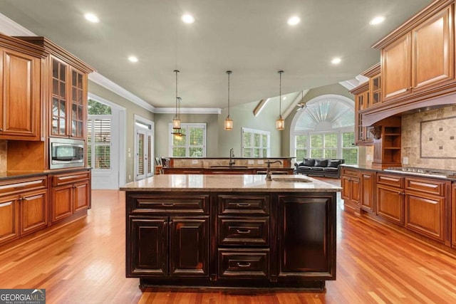 kitchen featuring sink, appliances with stainless steel finishes, decorative light fixtures, and a kitchen island with sink