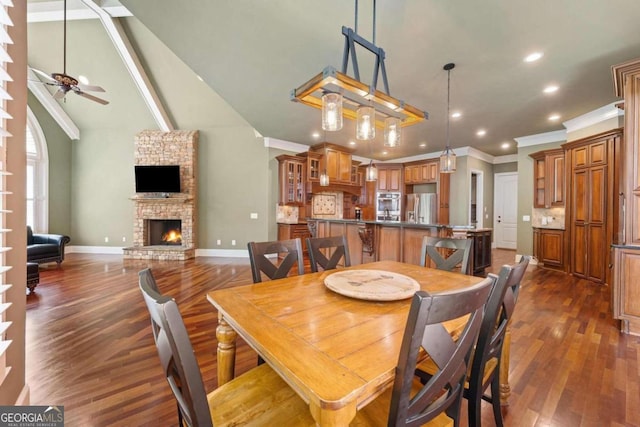 dining space featuring ceiling fan, high vaulted ceiling, dark hardwood / wood-style floors, ornamental molding, and a stone fireplace