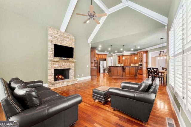 living room featuring a fireplace, high vaulted ceiling, ceiling fan, and light wood-type flooring