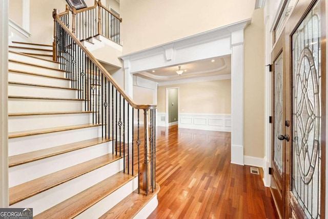 entryway with a high ceiling, wood-type flooring, ornamental molding, and a tray ceiling