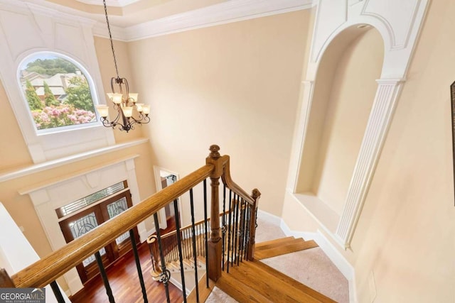 stairs featuring hardwood / wood-style flooring, ornamental molding, and a notable chandelier