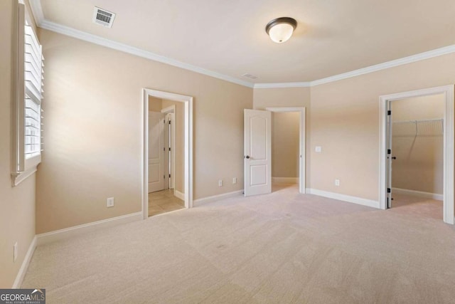 unfurnished bedroom featuring crown molding, a walk in closet, and light colored carpet