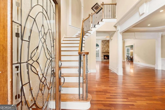 foyer featuring ornamental molding, hardwood / wood-style floors, a brick fireplace, and a high ceiling