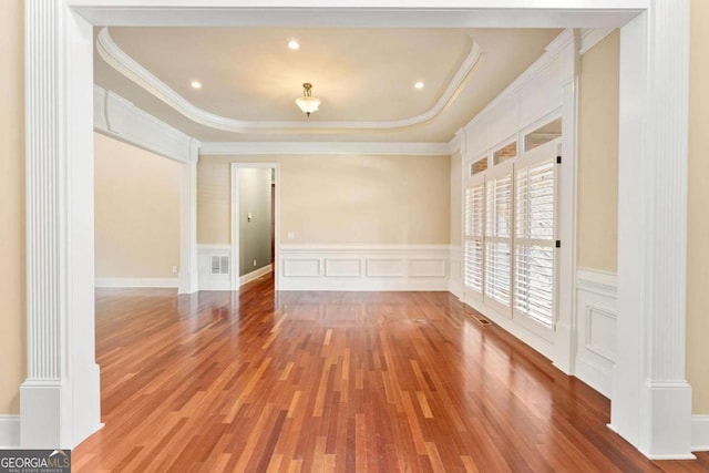 empty room with crown molding, wood-type flooring, and a raised ceiling